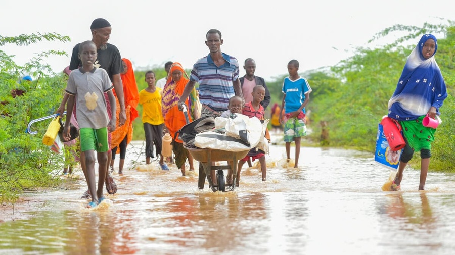 A man pushes a handcart containing a young child and his belongings through floodwaters accompanied by other family members.