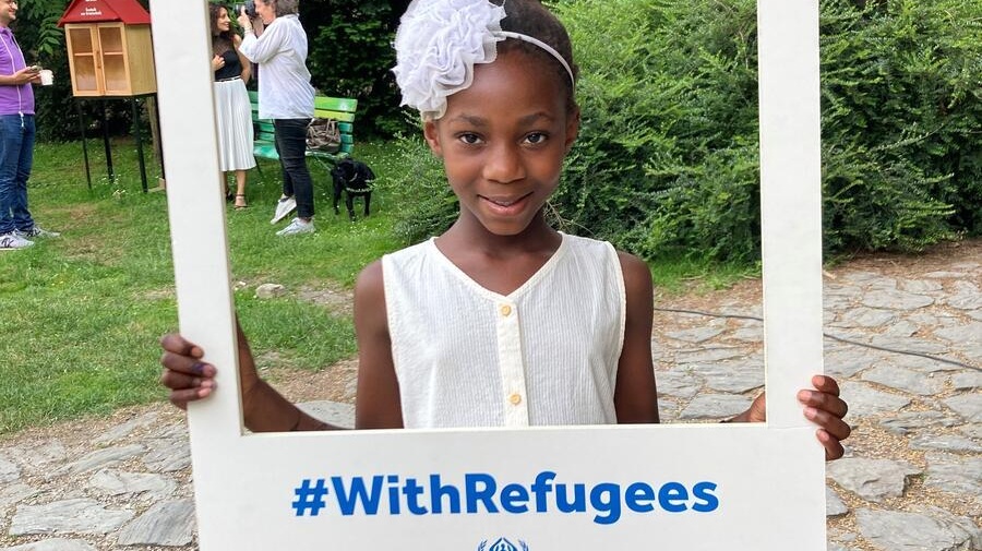 A girl stands outdoors holding up a #WithRefugees frame around herself