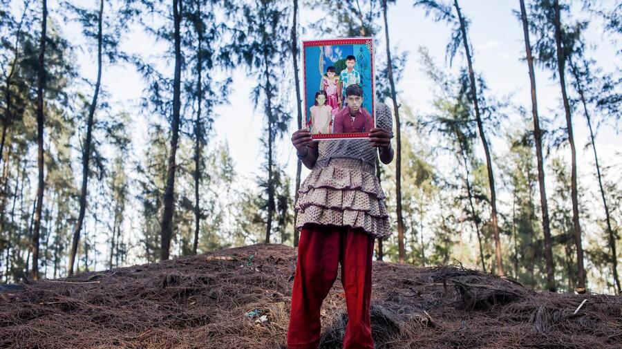 A young girl holds in front of her a photo of her lost 15-year-old brother.