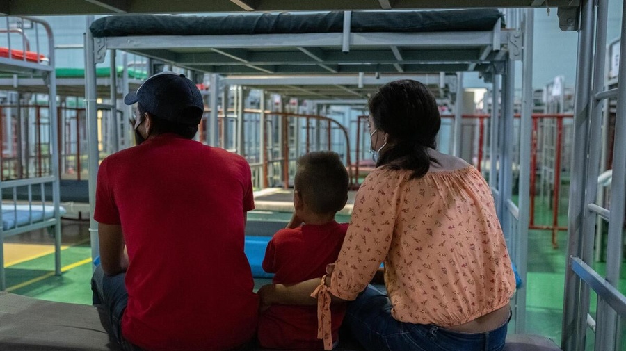 Honduran returnees sitting on a bed in the Kiki Romero gymnasium, a space enabled by the local government to provide care to people under Title 42.