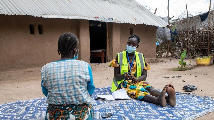 UNHCR partner sits on the floor and talks with a refugee woman