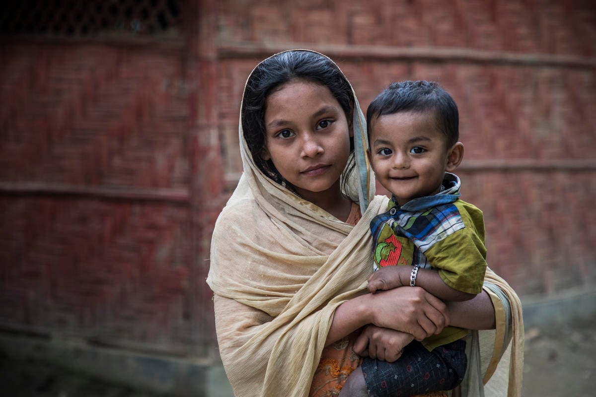 A young Rohingya girl holds her little brother