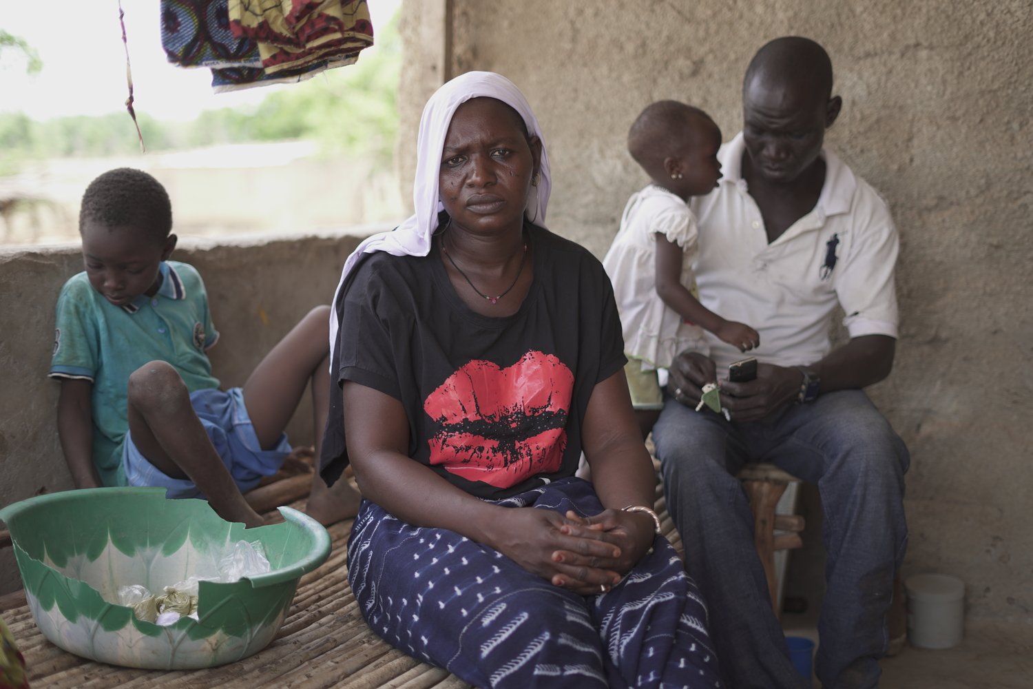 A woman sits staring into the camera while two small children and a man sit behind her.