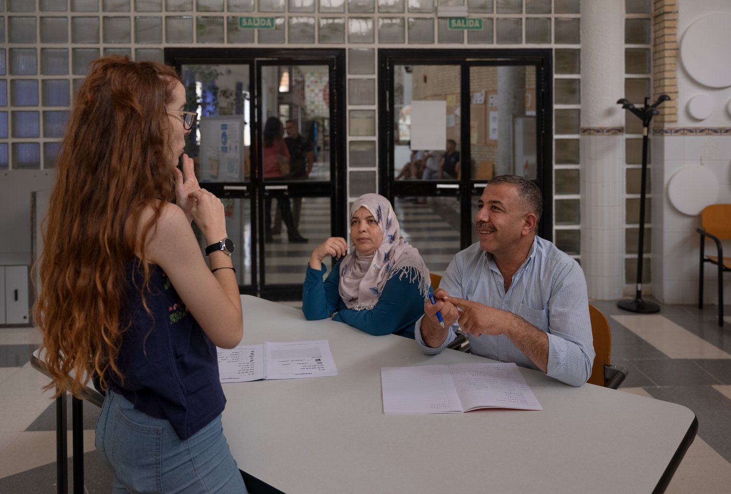 A couple seated at a table interact with their teacher standing in front of them.