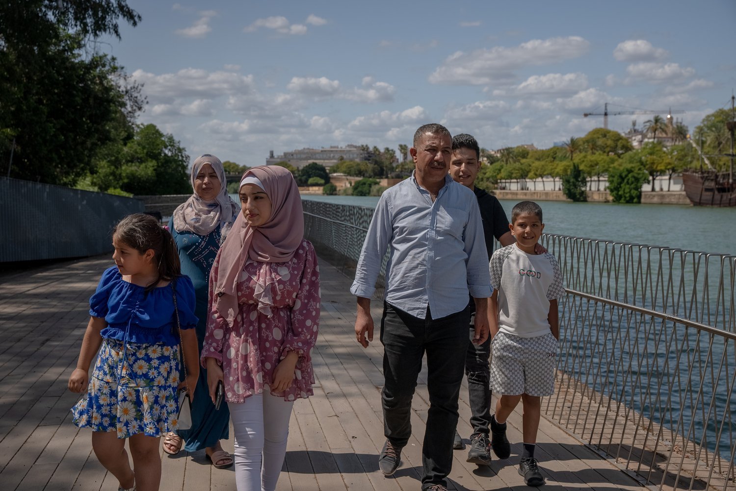 A couple and four children walk along a boardwalk next to a river.