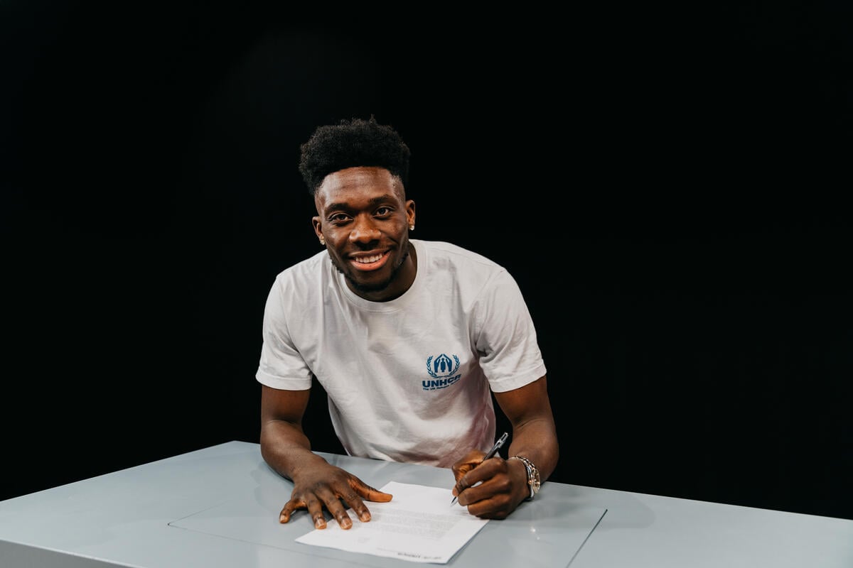 Alphonso Davies smiles at the camera while signing a contract.