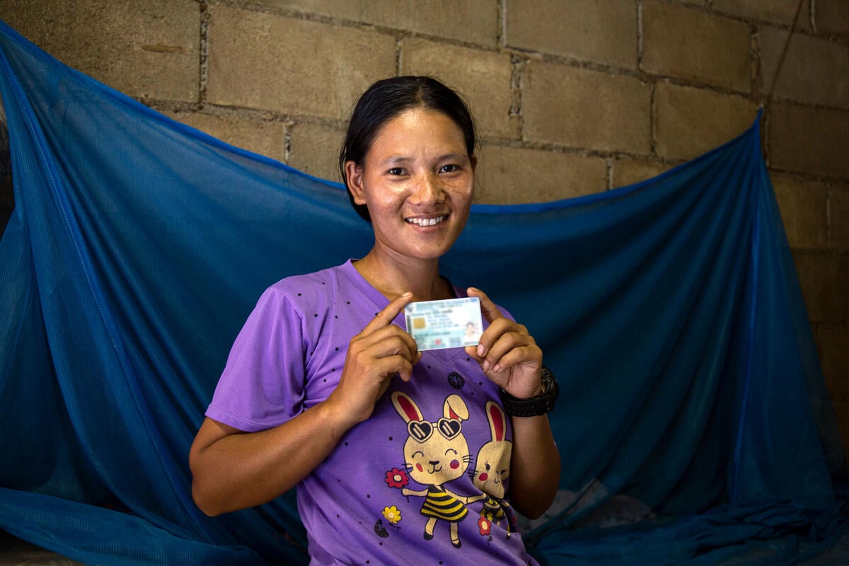 A woman holding an ID card in both hands smiles at the camera