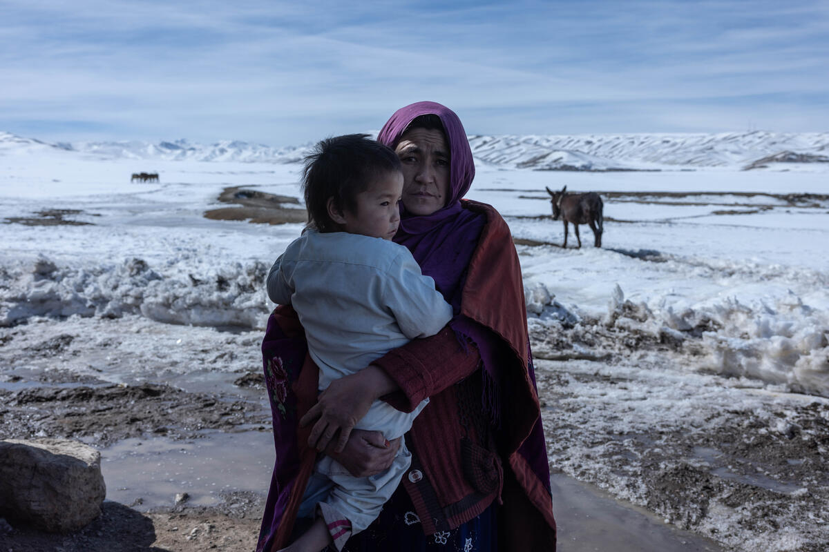 A woman stands in a snowy field holding a young child.