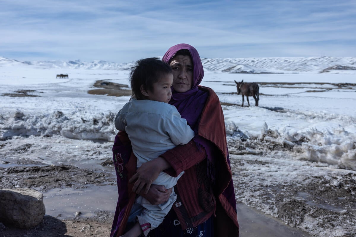 A woman stands in a snowy field holding a young child.