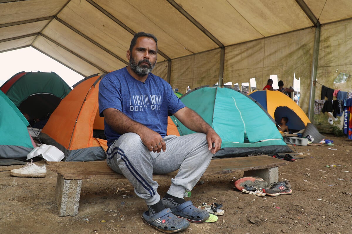 A man sits on a low bench in front of some tents.