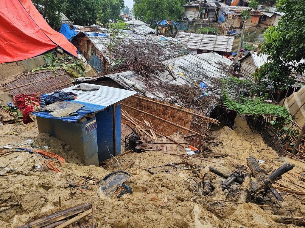 A damaged refugee camp, following landslides and monsoon rains. There is mud, tree branches and damaged buildings.