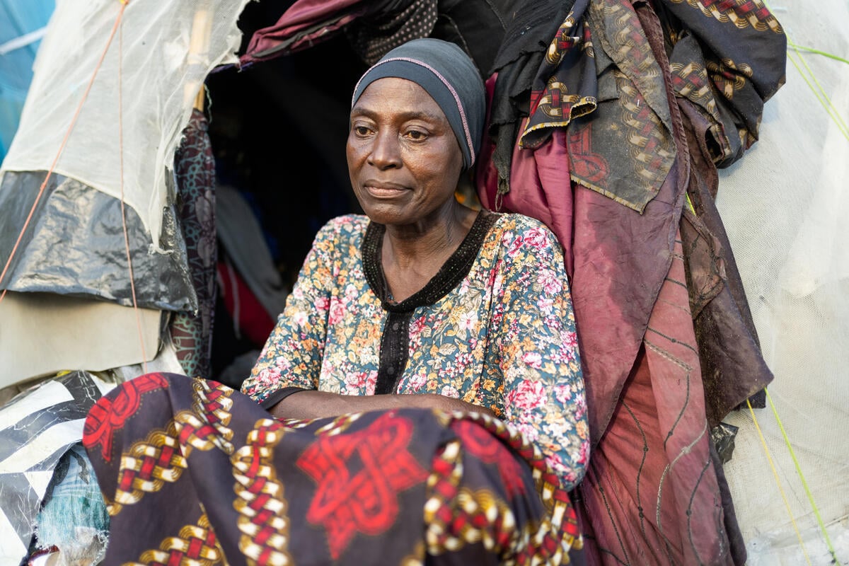 A woman sits in front of a makeshift shelter.