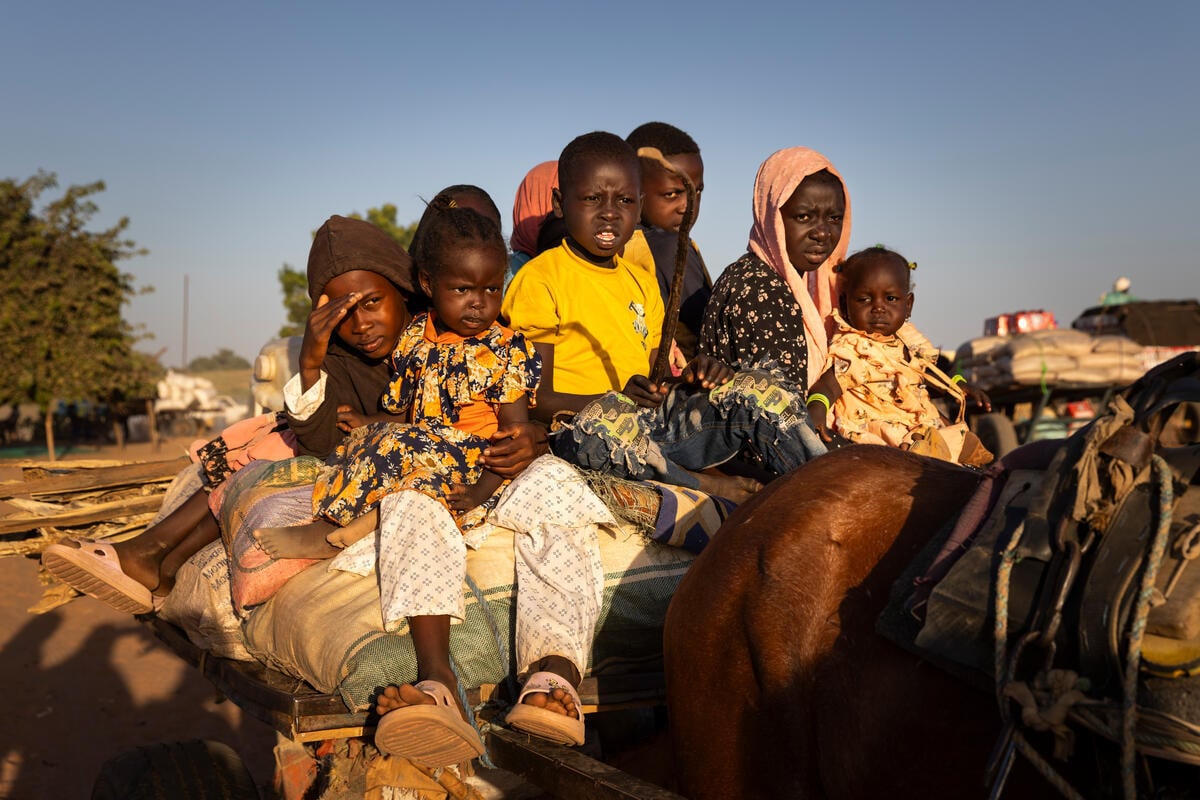 A group of Sudanese children sit on top of a cart behind a horse.