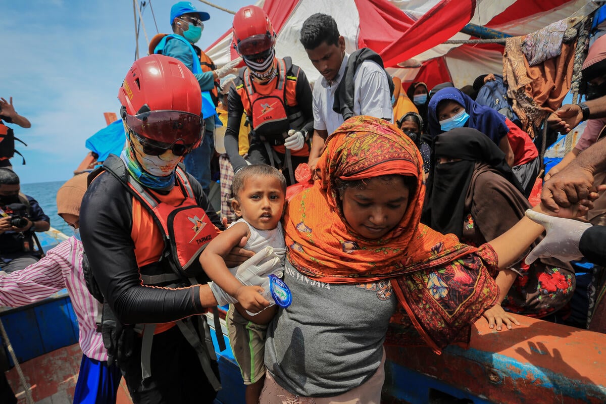 A rescue worker helps passengers disembark from a crowded boat.