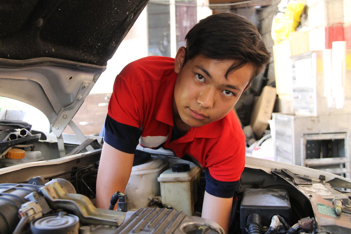 Iran. A young Afghan refugee apprentice practice his mechanic repair skills