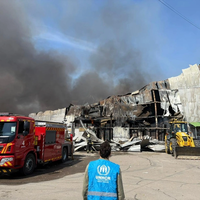 UNHCR staff member looks on as emergency workers work to put out a fire.