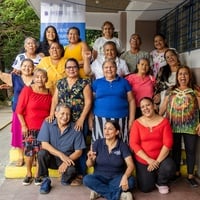 Quince mujeres adultas mayores, dos mujeres jóvenes, y un hombre adulto mayor, posan para la foto a las afueras de un aula