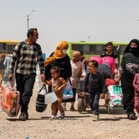 An Afghan family carries their belongings, walking away from two buses behind them.