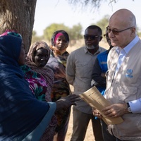 Barham Salih speaks to refugees and community members outside beside a large tree