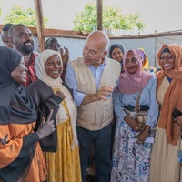 A group of men and women smile while standing and talking in an outdoor shaded structure
