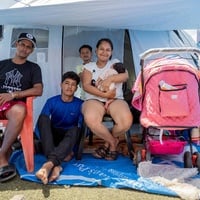 A family sits outside the entrance to a tent