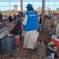 UNHCR staff support displaced families gathered in a large shelter with a sand floor