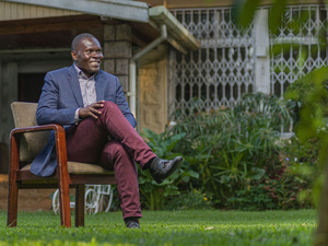 A smiling man sits on a chair in a garden