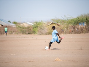 A girl prepares to kick a football on a dusty pitch.