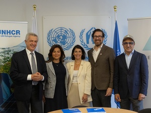 Five people smile and pose for the camera behind a table, with UNHCR banners in the background.