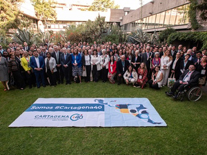 A large group of people pose for a group photo on a lawn with a banner in front.
