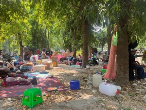 Families gather in the open under trees with their belongings.