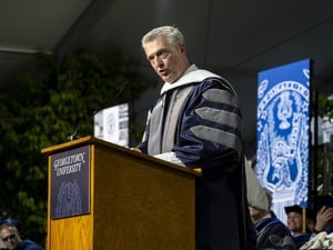 A man wearing ceremonial robes speaks at a lectern on stage