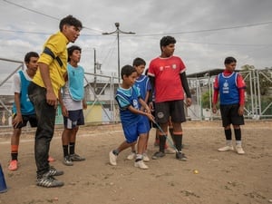 A young boy hits a yellow ball with a golf club as a group of children look on