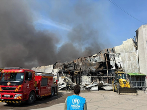 UNHCR staff member looks on as emergency workers work to put out a fire.