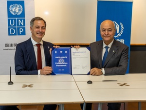 Two smiling men sit at a table, holding up a signed document that reads "UNDP-UNHCR Joint Collaboration Agreement: 2026-2030". Behind them are UNDP and UNHCR banners.