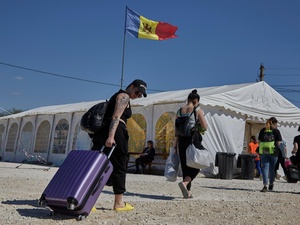 People carrying bags and pulling suitcases walk towards a large tent with a Moldovan flag flying above it