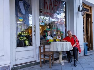 A smiling woman seated at a table in front of a café with colorful paintings on the windows and doors.