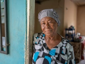 An older woman stands in the doorway of a house.