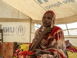 A woman sits on a yellow bed inside a UNHCR tent.