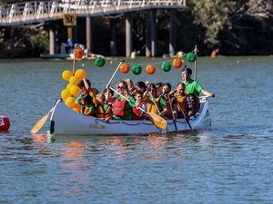 Men, women and children paddle a canoe decorated with green and orange paper lanterns and balloons.