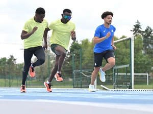 Three athletes run in parallel on a blue running track.