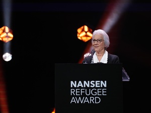 A woman stands on stage behind a podium bearing the words 'Nansen Refugee Award'