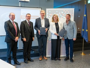 Four men and one woman stand looking at the camera while holding up two documents