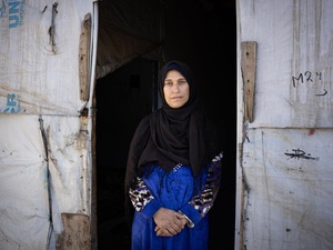 A woman wearing a headscarf stands at the entrance to a UNHCR-branded shelter.