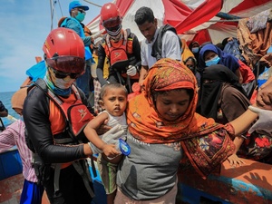 A rescue worker helps passengers disembark from a crowded boat.
