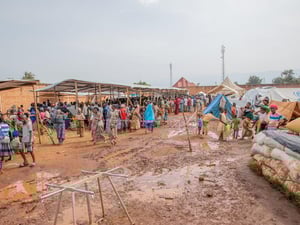 Large groups of people gather in the mud under makeshift shelters
