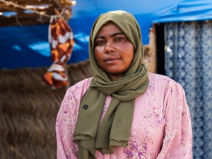 A portrait of a woman wearing a green headscarf standing in front of a shelter.