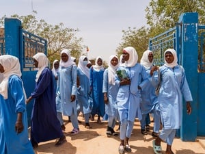 Female high school students carrying books and bags walk through school gates.
