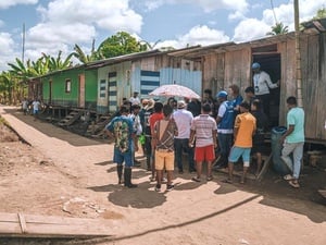 UNHCR staff among a group of people gathered outside a wooden shelter in a row of similar structures.