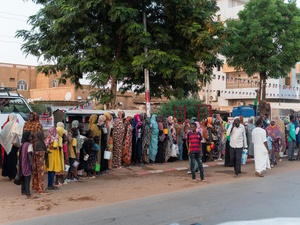 Families from El Fasher queue outside along a street.